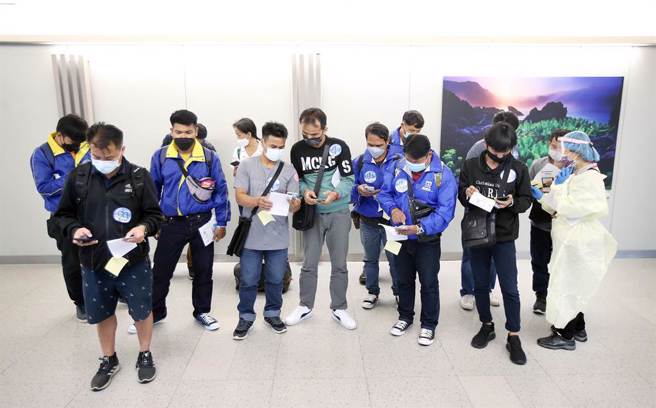 劳动部宣布10月13日起接种过2剂疫苗的移工一律适用「0＋7」新制。在桃园机场第一航厦入境管制区内，身穿防护衣的劳动部人员协助刚下机的移工填写资料。（范扬光摄）