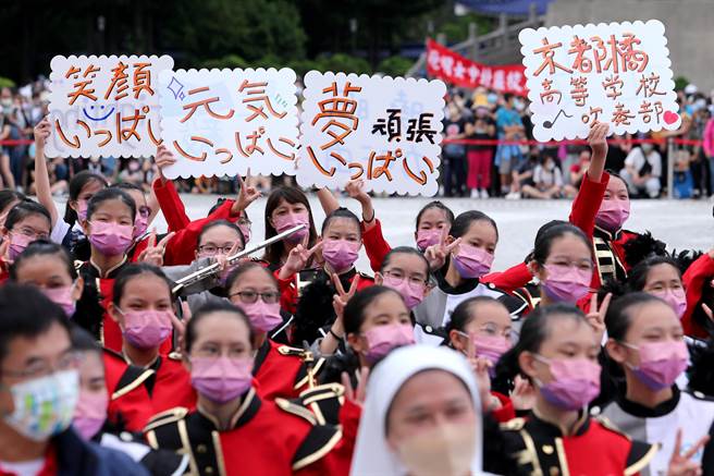 来台参加国庆大会的日本京都橘高等学校吹奏乐部，所到之处刮起一阵「橘色旋风」，9日他们与北一女中乐仪旗队、台中晓明女中管乐团在台北市自由广场一同交流演出，台中晓明女中的学生自制日文看板欢迎京都橘高校吹奏乐部来台演出。（资料照／黄世麒摄）