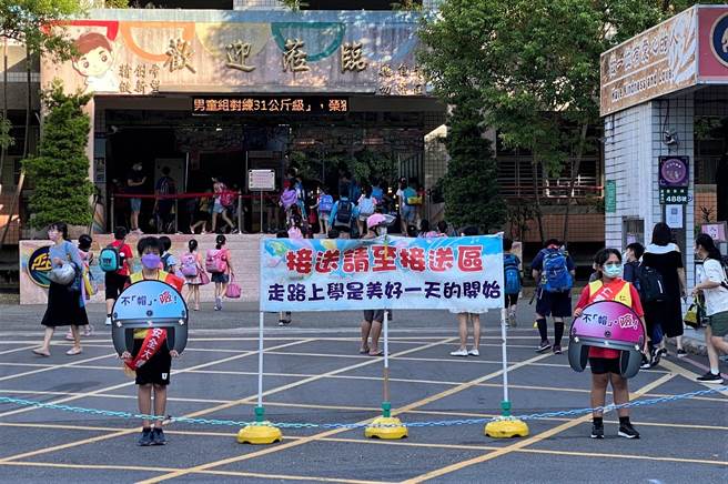 仁爱国小学生干部轮流担任安全帽大使，举牌并运用音箱广播，提醒「家长及同学骑乘机车请戴安全帽，您的孩子需要安全」。（新北市教育局提供）