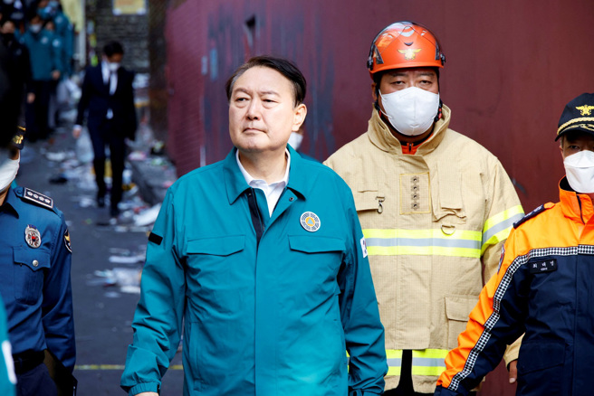 南韩首尔梨泰院29日深夜发生踩踏事件，酿成151人丧命，龙山区消防局长崔成范（上图后方戴橘色安全帽者）彻夜未眠指挥、在记者会上冷静通报救援进度，引发好评，不过眼尖网友捕捉到他说话时，拿着麦克风的手不断颤抖，似乎也被这起意外的规模吓到。图为30日崔成范陪同南韩总统尹锡悦视察灾区。（图／路透社）