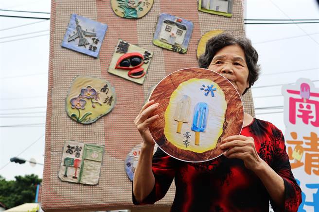 参与创作的长辈拿着印有自己作品的看板在大冰棒前合照。（吕妍庭摄)