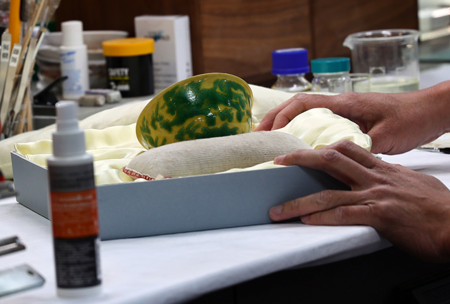 故宫发生文物毁损问题，引发关注，立法院教育及文化委员会7日前往故宫考察，文物修护师正专注地修復弘治款娇黄绿彩双龙小碗。（刘宗龙摄）