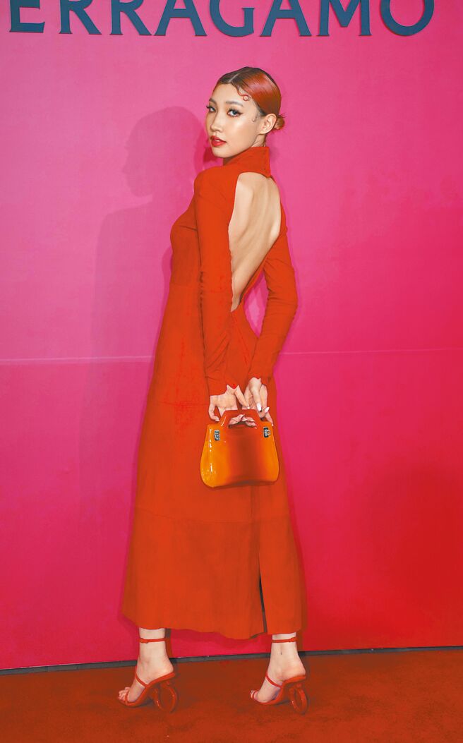 Karencici身穿橘红色贴身洋装，背面挖空设计性感十足。FERRAGAMO Gancino造型跟饰高跟鞋4万5900元、红色麂皮长洋装19万9000元、夕阳渐层色迷你手提包6万9900元。