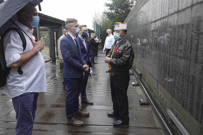 來台參加二戰受難戰俘追思會的各國人士，在刻滿戰俘名單的紀念牆前聽取資深退伍人員解說。（黃子明攝）