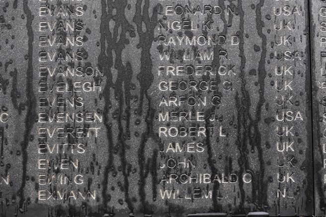 由於當地上午下著間歇雨勢，刻滿戰俘名單與國籍資料的碑體牆面留下一條條清晰雨痕。（黃子明攝）