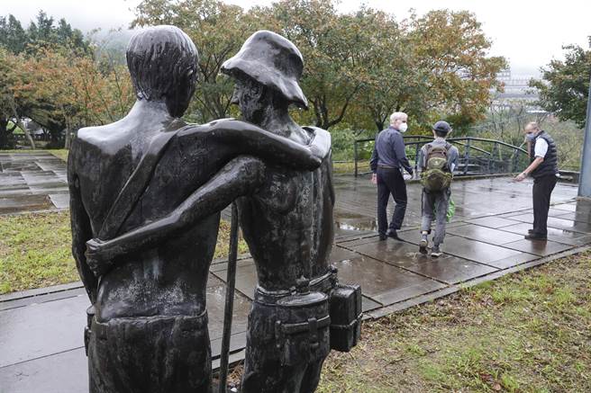 金瓜石「國際終戰和平紀念園區」戰俘名單與國籍資料的紀念牆前，豎立寓意戰俘相扶持的「Mates」（夥伴）的銅雕作品。（黃子明攝）