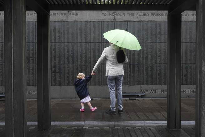 新北市金瓜石山區的「國際終戰和平紀念園區」13日舉行二戰受難戰俘追思會，帶著小孩的家屬在刻滿名單的紀念牆上找尋先人名字。（黃子明攝）