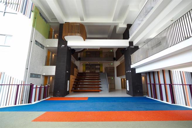 社宅二楼的大平台创造出近十米挑高的半户外公共空间，铺设亮眼的橡胶地皮，是居民互动游憩的场地。（图／林格立）