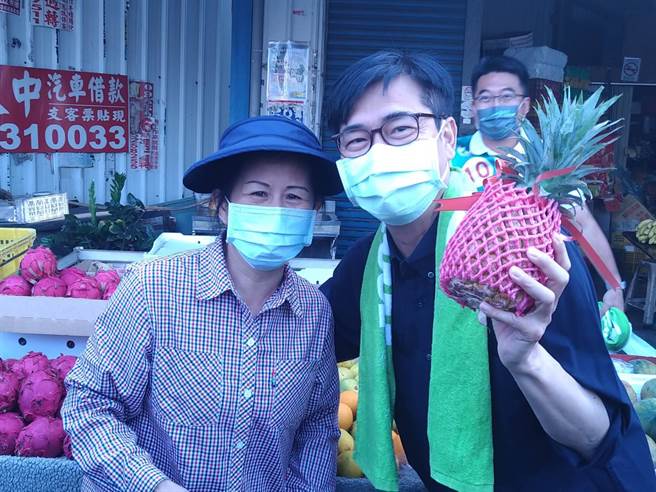 民進黨高雄市長候選人陳其邁勤走基層，一早到大社果菜市場拜票，獲得選民熱情回應，經營水果攤的阿嬤當場贈送陳一棵鳳梨，祝福陳其邁高票「凍選」。(林雅惠攝)