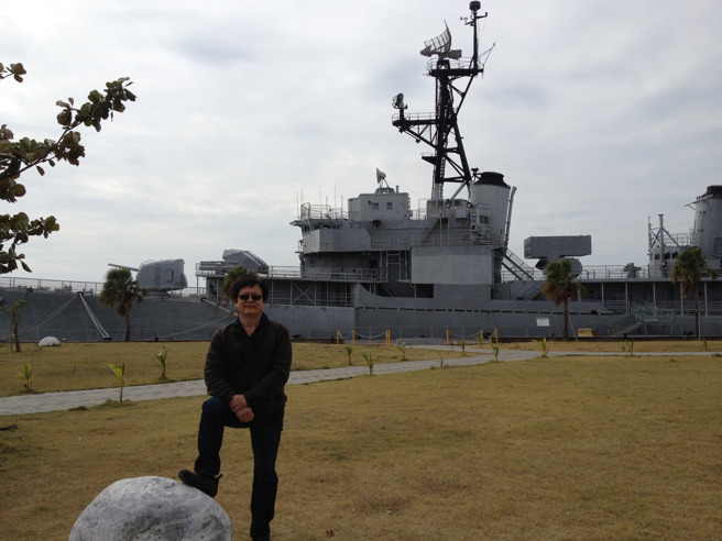 陸大哥與停泊安平港畔的德陽艦合影。艦艏A炮位為五寸艦炮，其後B炮位為雄風一型飛彈發射器和魚雷發射管，艦中煙囪後方為ASROC反潛火箭。（圖文：劉良昇）