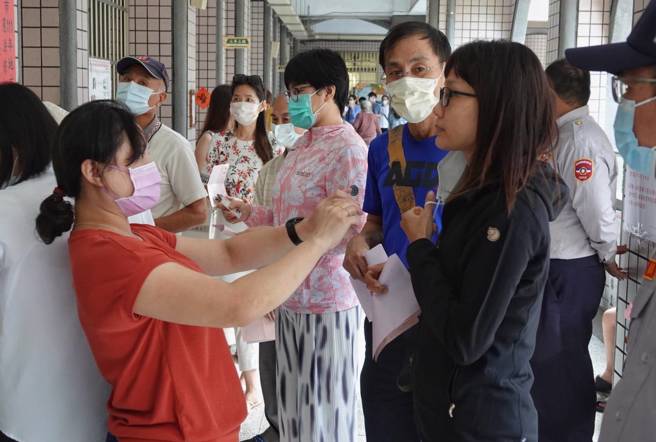 九合一選舉上午開始投票，選務人員依規定核對選民身分及量體溫。（黃子明攝）