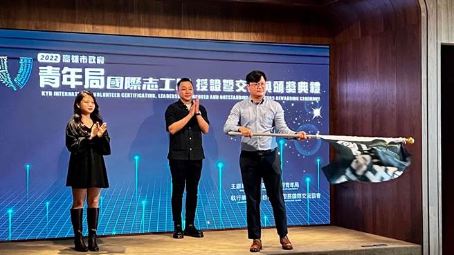 高市青年局局长张以理与新任团长挥舞团旗，象徵志工团的服务精神持续传承。（柯宗纬摄）