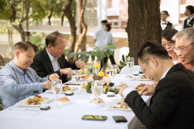 （国立高雄餐旅大学校长陈敦基(左排一)和来宾，品嚐香蕉花植物鱼肉松露风味麵疙瘩佐荷兰酱柑橘。图／高餐大提供）