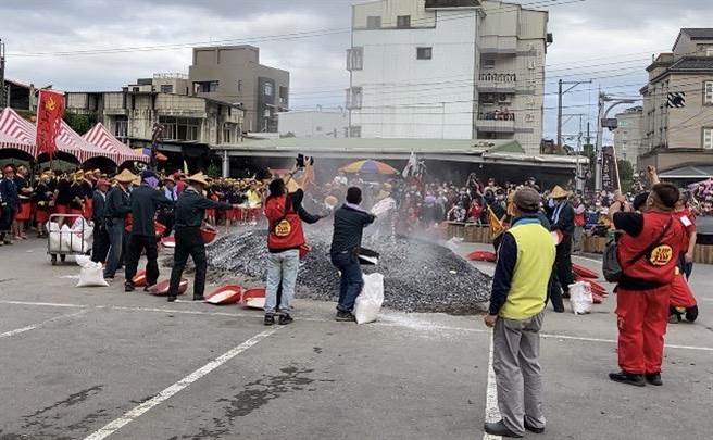 庙方工作人员不断在炭火堆上洒盐与白米，不停发出劈哩啪啦声响，表示降温及象徵神明加持，以形成一股无形的庇佑力量，让伙伴们过火过程中能确保安全。（吴佩蓉摄）