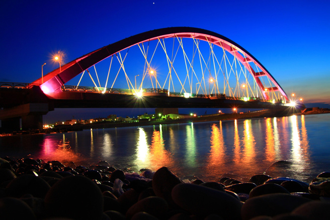 竹围渔港北边入口的彩虹桥是在地一大地标，主桥单跨180公尺、高31公尺相当吸睛，入夜点灯后浪漫气氛满点。(图／桃园区渔会)

