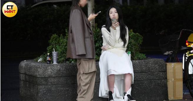 外型姣好的美麗妄娜在友人陪伴下，坐在路邊花台上滑手機。（圖／本刊攝影組）