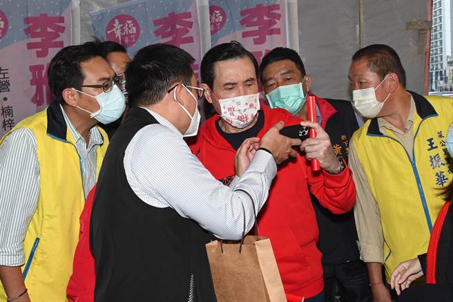 前總統馬英九（右二）8日傍晚到左營區自由路黃昏市場發送春聯，適逢台北市立委補選結果出爐，隨扈拿手機給他觀看選情。（林瑞益攝）