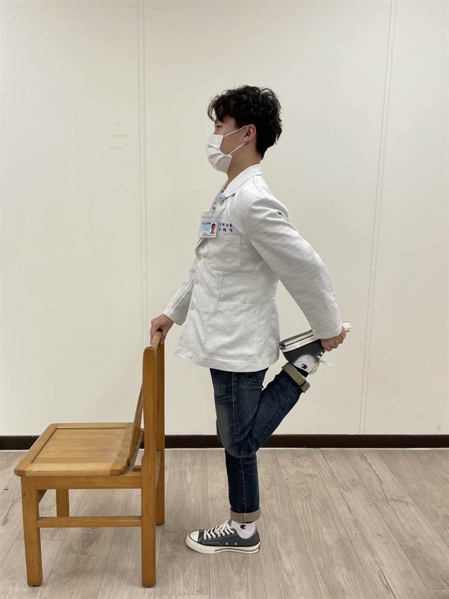 利用椅子维持平衡，单脚站立用手扣住另一脚向上弯曲，进行大腿前侧的股四头肌伸展运动。（卫福部苗栗医院提供／李京升苗栗传真）