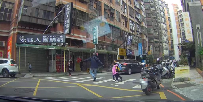 日前脸书上一名网友上传一段影像至社群「林口大家庭」，影像中2名幼童行经林口区一处无号志路口时，因车流眾多，2名幼童在路边徘徊不敢通行，一名机车骑士见状便把车停下，下车带着2名幼童过马路。（图片授权／民眾提供）