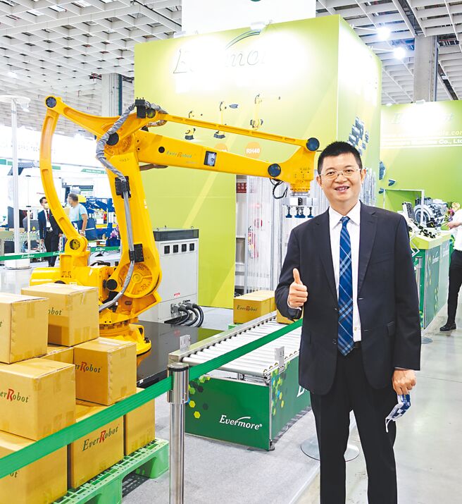 勤堃机械总经理廖河诚，和该公司机械手臂合影。图／黄俊荣
