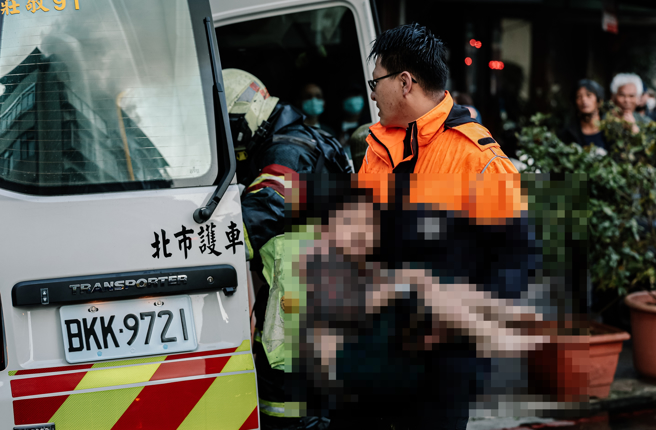 台北市信义区和平东路3段巷弄内一栋五楼公寓10日清晨发生火警并向顶加延烧，警消到场时已全面燃烧，经射水抢救，消防人员在后阳台救出2名学童，但孩童父亲受困顶加屋内不幸罹难，母亲因人在国外逃过一劫，详细起火原因待调查；车窗映射遭祝融的房屋，甫被救出的学童饱受惊吓在救护人员怀中痛哭。（郭吉铨摄）