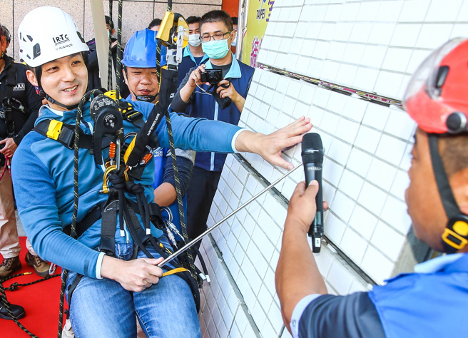 台北市长蒋万安（左）10日上午赴市府第二行政大楼，出席劳动检查处与绳索同业缔结安全伙伴的结盟活动。会中他穿戴背负式安全带、安全帽，亲自上场体验，用绳索攀爬对外墙进行检测，体验作业之辛劳。（粘耿豪摄）