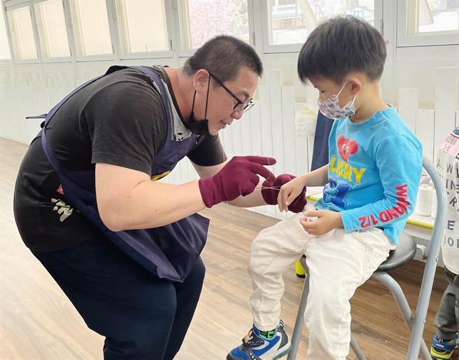 老师在小朋友的手上示范挽面的动作。(台中市政府提供)