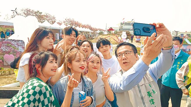 图为台南市长黄伟哲在花旗木大道前与年轻人玩自拍。（程炳璋摄）