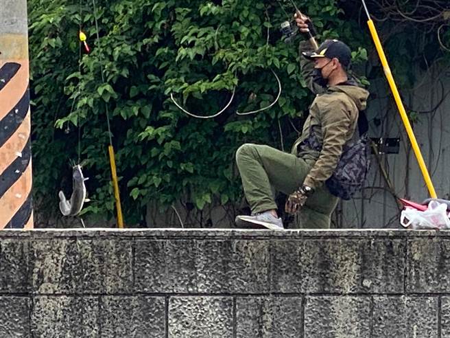 移工坐在石笱排水护岸垂钓，见鱼儿上钩再跳回岸边。（孙英哲摄）