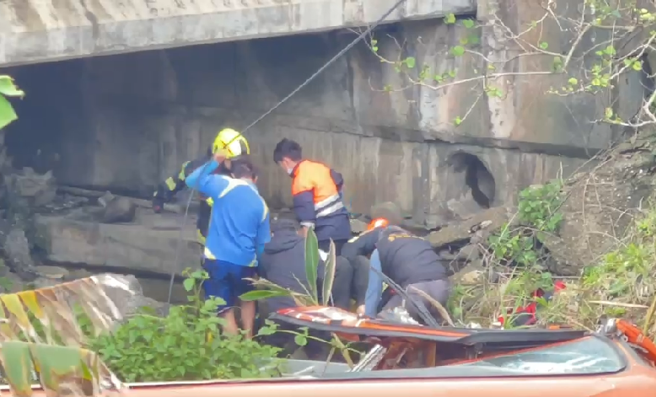 现场画面曝光，只见整辆客运横躺在桥下，挡风玻璃喷飞，车身疑似悬空，两侧车身卡在树丛中，数名搜救人员在客运下方的溪中用担架抬出喷飞的伤者。（丰滨乡公所提供）