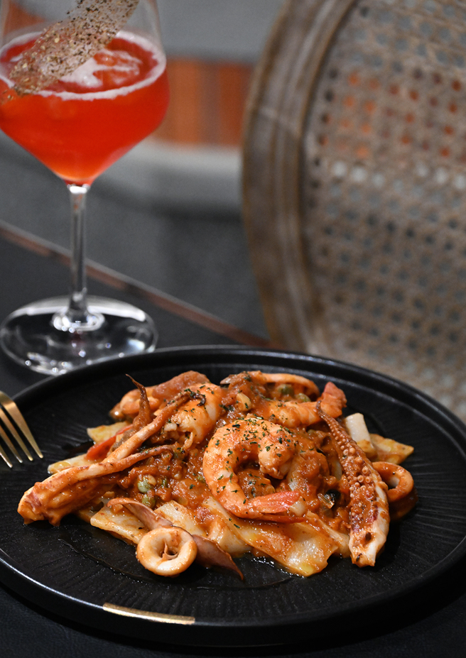 客家煙花女海鮮粄條為經典義大利麵創意延伸，以臺灣粄條取代義大利麵，搭配港口海鮮，番茄、橄欖和酸豆，口味道地。旁為以琴酒為基底，鋪陳草莓香料氣息的限定系列「草莓青花椒」。(攝影/Carter)
