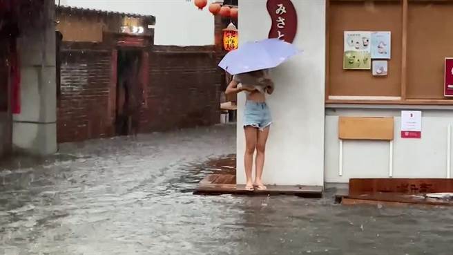 鹿港老街積水嚴重，一名女子站在門邊台階查看狀況。（民眾提供／孫英哲彰化傳真）