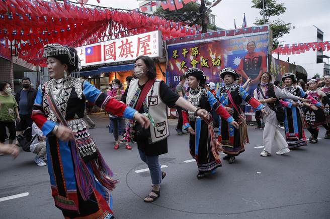 妇女穿上各民族传统族服参加踩街活动，沿路边走边跳舞经过忠贞新村着名的国旗屋。（黄子明摄）