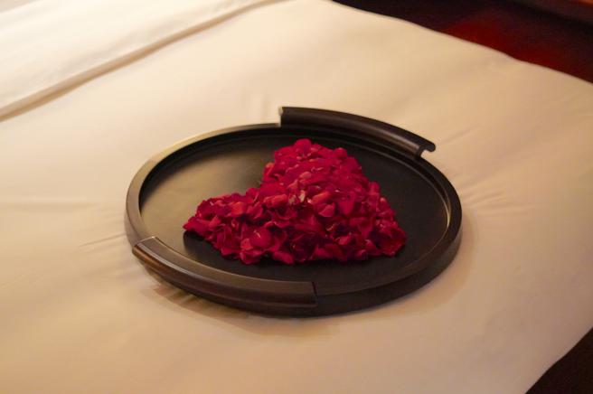 床铺上有满满红玫瑰花瓣的心型花堆。（何书青摄）
