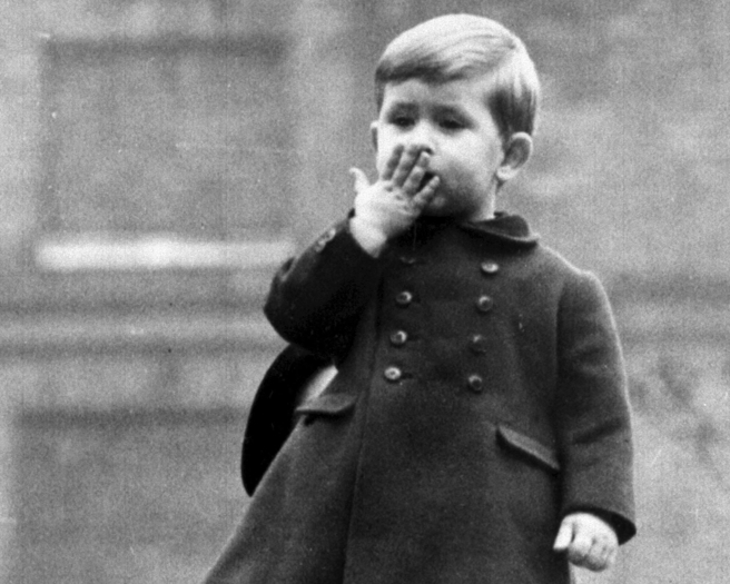 4岁的查尔斯1952年站在伦敦克莱伦斯宫（Clarence House）的围墙上，向国会开议大典（State Opening of Parliament）当天搭乘马车经过的母亲和祖父母发出飞吻的神情，当时乔治六世仍在位。（达志图库/TGP）