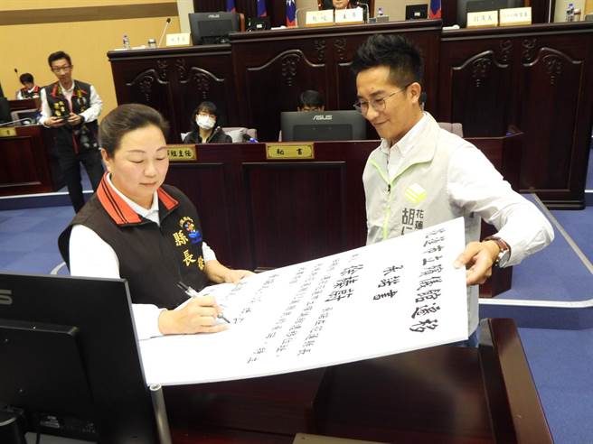 花莲县议员胡仁顺（右）今在县议会定期大会上，出示承诺书要求县长徐榛蔚（左）签署，承诺在任期内完成花莲花莲市立殡仪馆选址作业。（罗亦晽摄）