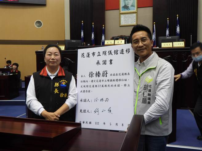 花莲县议员胡仁顺（右）今在县议会定期大会上，出示承诺书要求县长徐榛蔚（左）签署，承诺在任期内完成花莲花莲市立殡仪馆选址作业。（罗亦晽摄）