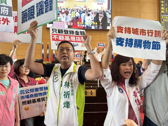 台中市议会为了购物节3.5追加预算，蓝、绿议员高举海报互呛。(林欣仪摄)