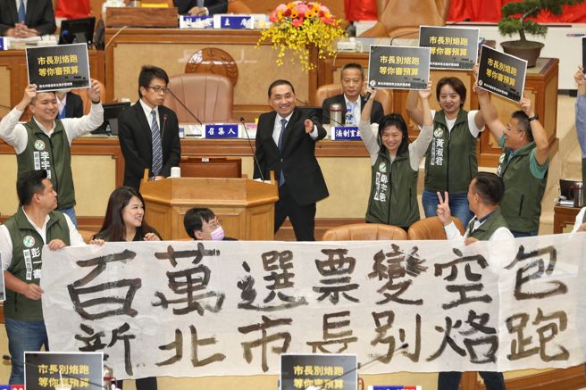 新北市议会12日举行市政总质询，民进党市议员一同对着新北市长侯友宜（中）高喊「百万选票变空包 新北市长别烙跑」并唱起「我等着你回来，你一定会回来」。（杜宜谙摄）