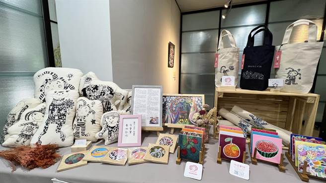 现场摆设有印制林依柔作品的牛仔布小物袋、杯垫、软雕塑布娃娃。（张毓翎摄）