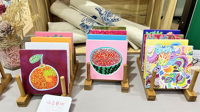 现场摆设有印制林依柔作品的牛仔布小物袋、杯垫、软雕塑布娃娃。（张毓翎摄）