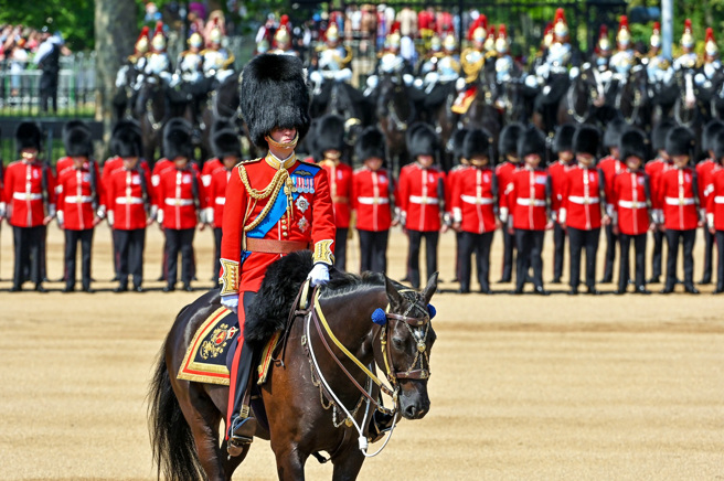 英国威廉王子10日在烈日下视察皇家阅兵仪式的最后彩排，过程中至少3名士兵热到晕倒、被抬走。图为穿戴熊皮帽视察的威廉，后排为参与彩排的禁军。（图／TPG、达志影像）