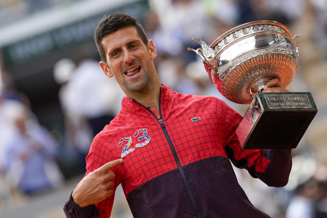 乔柯维奇一手拿着法网冠军奖杯，一手指着自己外套上「23」数字，代表他生涯打下了23座四大赛单打冠军。（美联社）