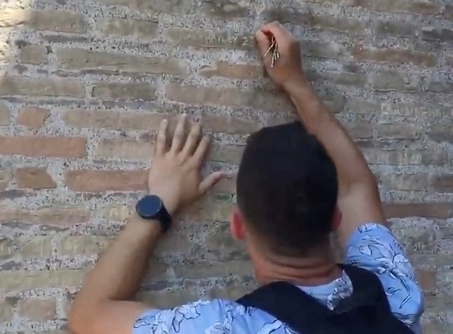 一名觀光客日前在羅馬競技場牆面刻字，旁人規勸不聽。義大利警方正在追查此人身份。（路透社）