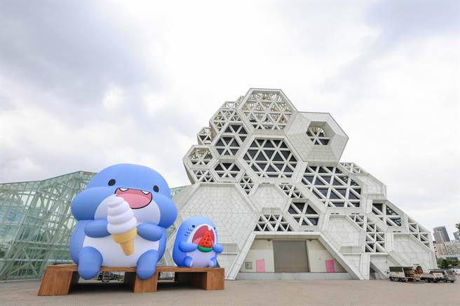 「胖鯊魚鯊西米」來了啦，在雪白高流音浪塔前，吃冰淇淋和西瓜的萌樣，實在很夏天。（擷取陳其邁臉書／柯宗緯高雄傳真）