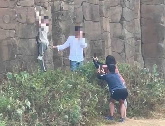 年輕的家庭遊客無視告示牌禁止，仍攀爬柱狀玄武岩演拍照。（翻攝爆料公社／許逸民澎湖傳真）