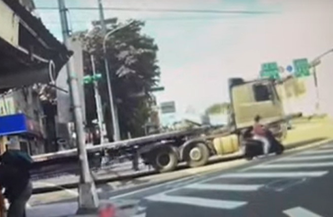 警員攔下連結車駕駛，而遭到「內輪差」捲入車底的婦人慢慢爬出。(影片翻拍)