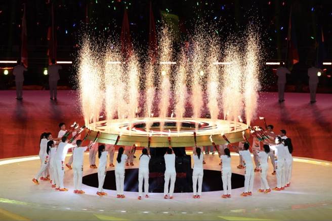 31名火炬手共同点燃的「太阳神鸟」图案圣火盘光芒四射，盘旋上升，引燃象徵太阳神鸟12道金芒的空中焰火，焰火传递，最终点燃场外的主火炬塔。（新华社）