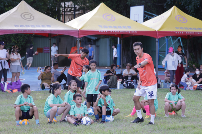 台北亲子足球营热闹展开，图为担任教练的台湾石虎足球队后卫谭珷龄指导小朋友踢球，家长则在后方帐篷休息避暑。（台北市体育会足球协会提供）