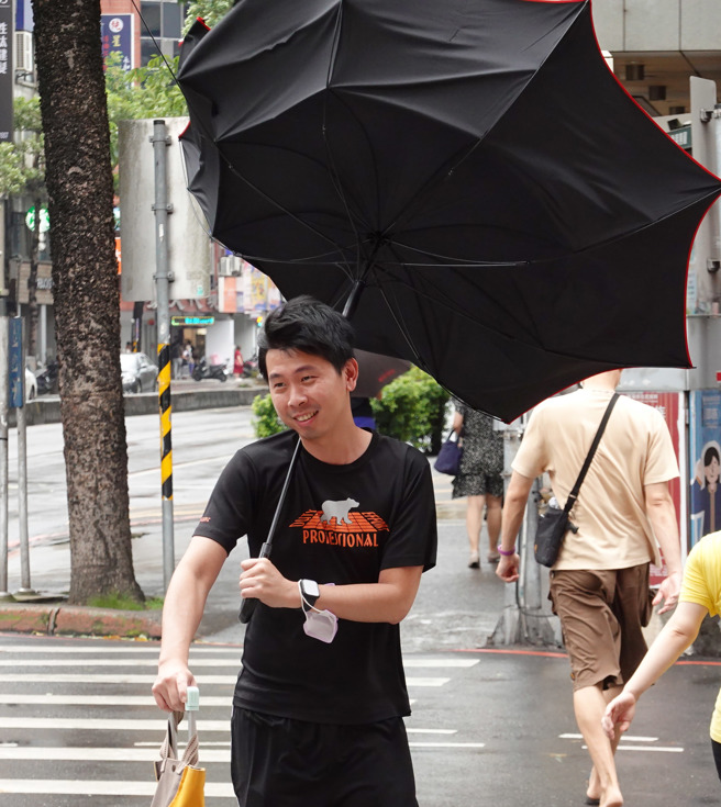卡努颱風來襲，3日白天雨勢不大，但風勢忽強忽弱，突然而至的強風襲來讓民眾措手不及，抵著雨傘禦風前行。（姚志平攝）